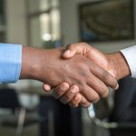 Two people shaking hands across a meeting table after agreeing a deal