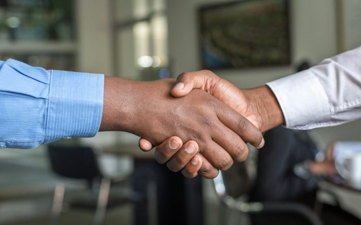Two people shaking hands across a meeting table after agreeing a deal